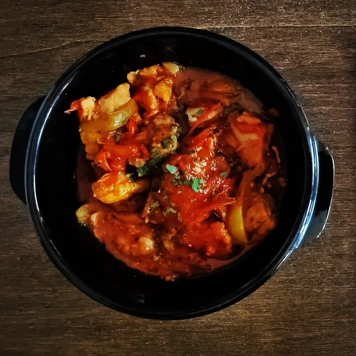 Un tegame nero di spezzatino al pomodoro con patate e peperoni, visto dall'alto sul legno.