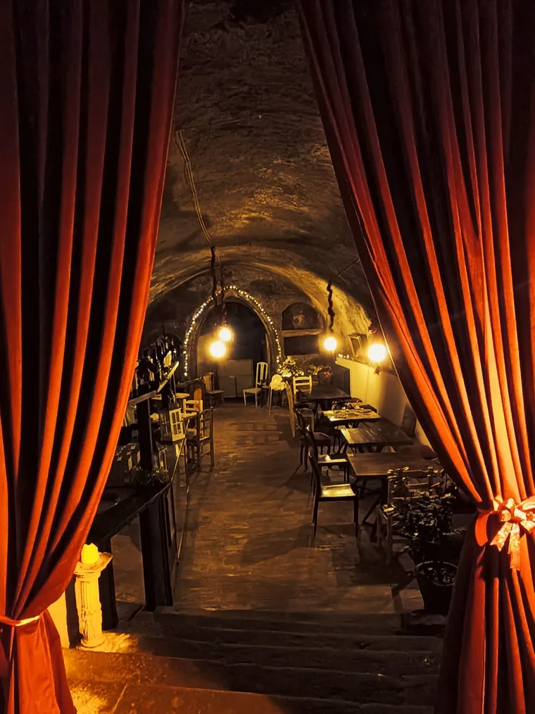 Una tenda di velluto arancione scostata su una sala più interna, illuminata da lampade basse sotto la volta.